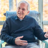 Smiling older man in a black sweater sitting in a chair, discussing home selling experiences, reflecting Zoom Casa's customer satisfaction and support.