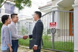 Couple shaking hands with a real estate agent in front of a house for sale, emphasizing quick home sales and value-driven solutions.