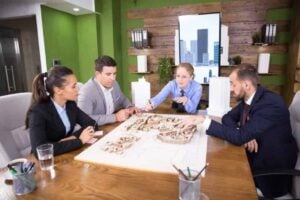 Group of professionals discussing strategic home upgrades around a model layout in a modern office setting, emphasizing collaboration for attracting wealthy buyers.