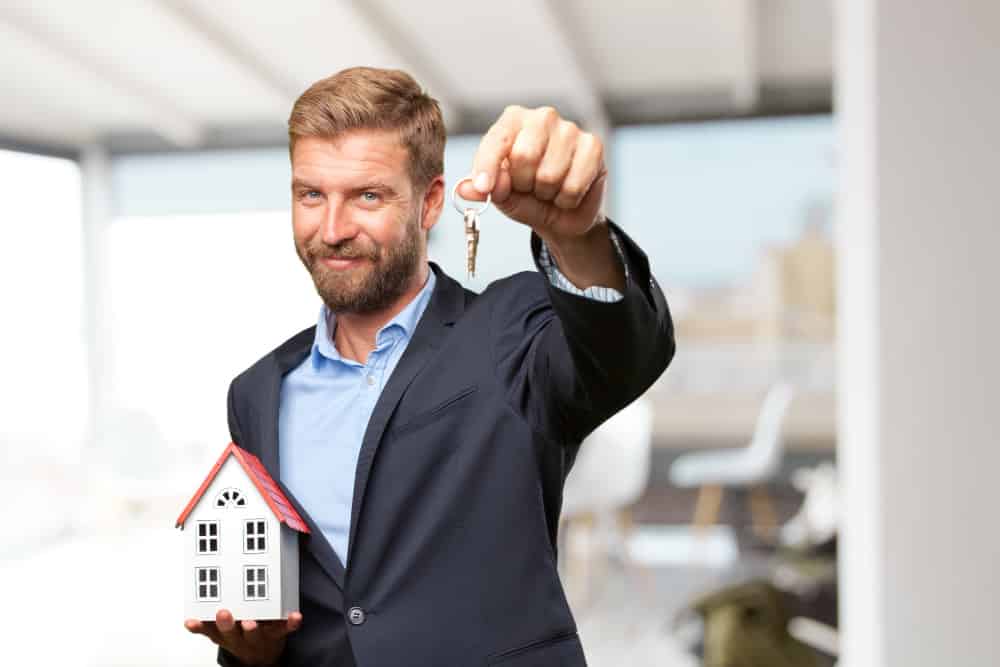 Man in a suit holding a miniature house and keys, symbolizing home sales and real estate solutions for quick transactions.